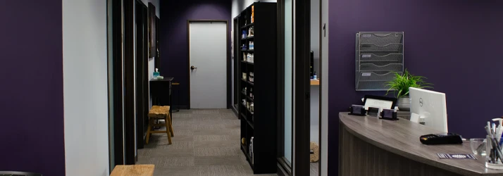 Interior hallway with treatment rooms, shelving units, seating benches, and a curved reception counter.